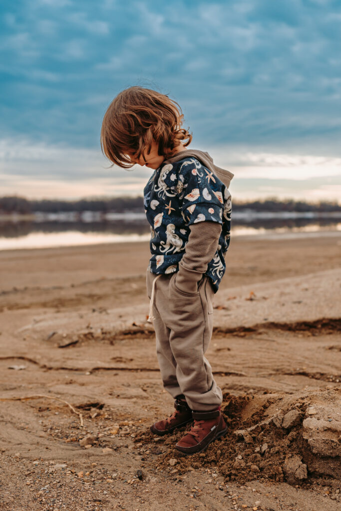 Little boy kicking sand standing on a beach in front of a beautiful cloudy sky 