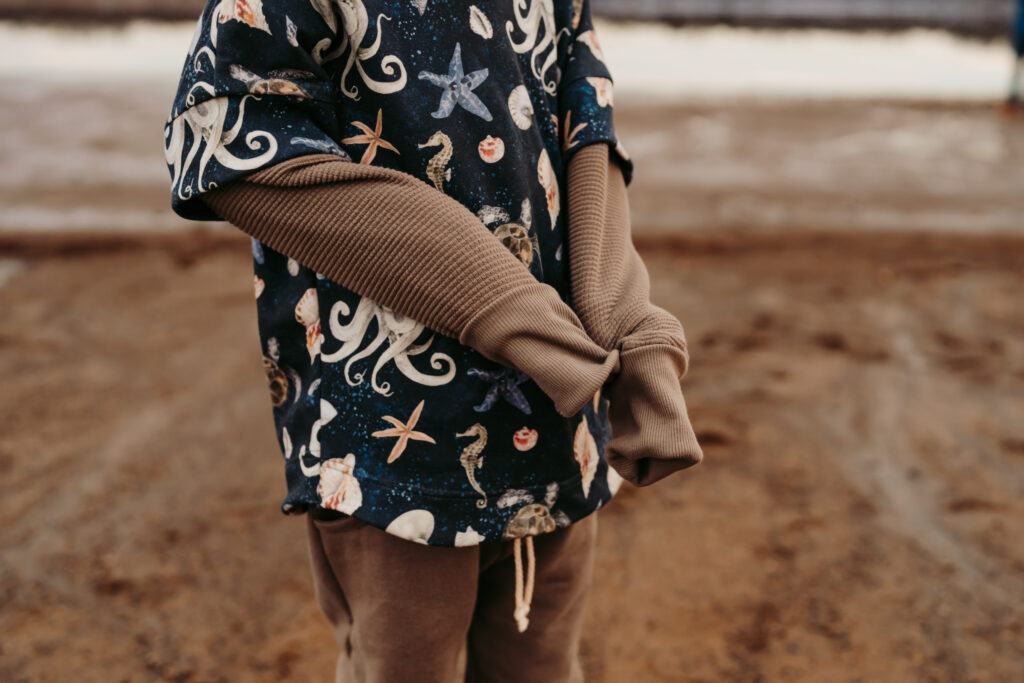 Close up of a little boy wearing a sweater with prints of octopus, seashells, seahorses and star fish on the sweater