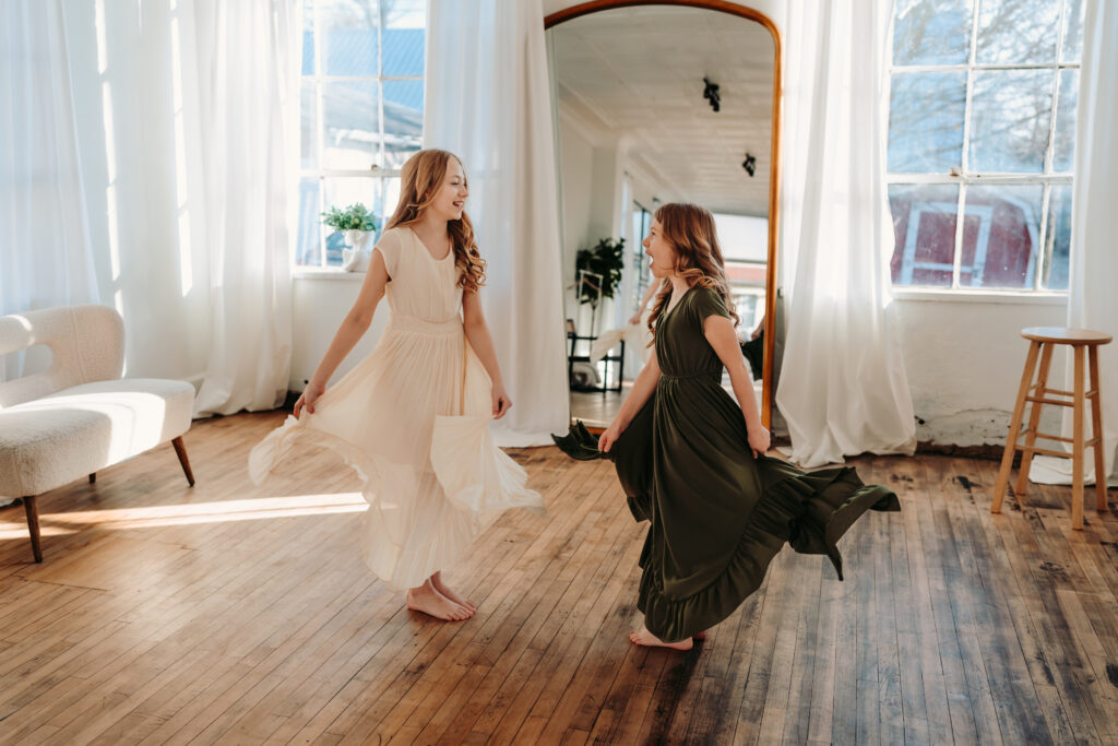 Two sisters look at each other while dancing in a studio in front of a full length mirror
