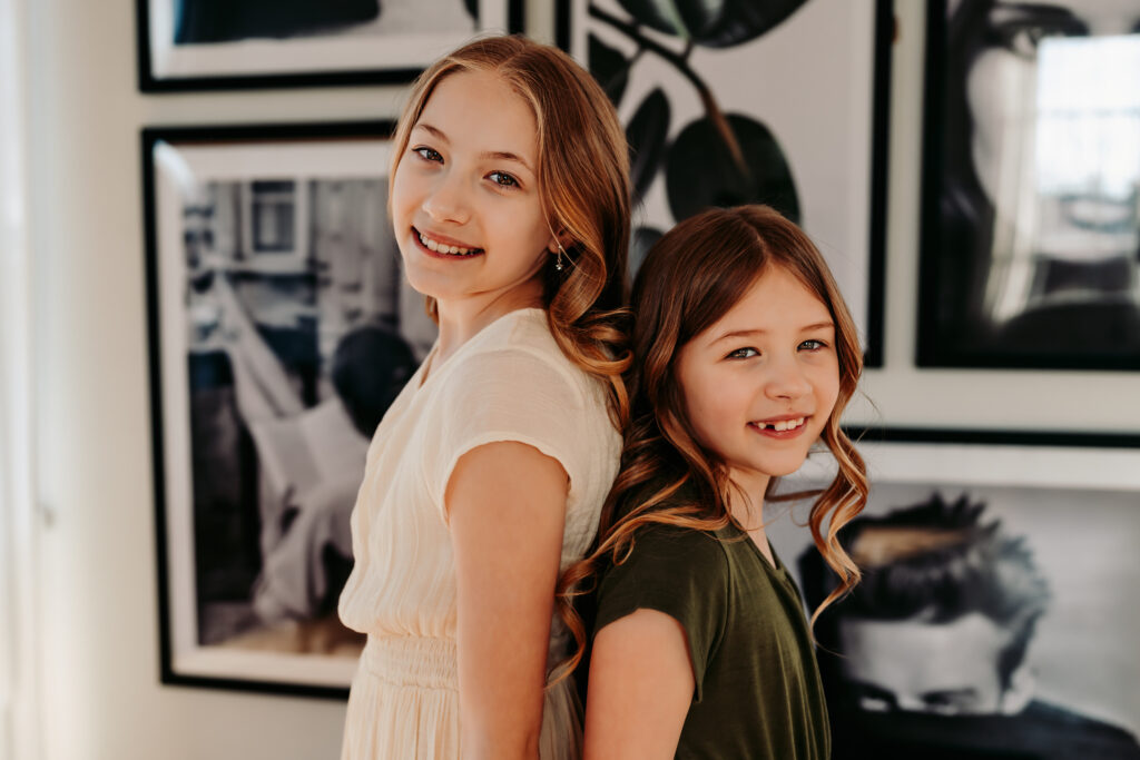 Two sisters standing back to back looking at the camera and smiling