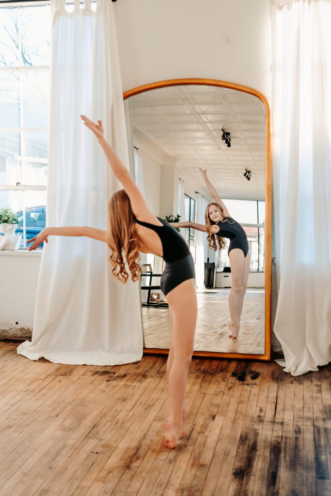 Dancer strikes a dance pose in front of a full length mirror while watching herself